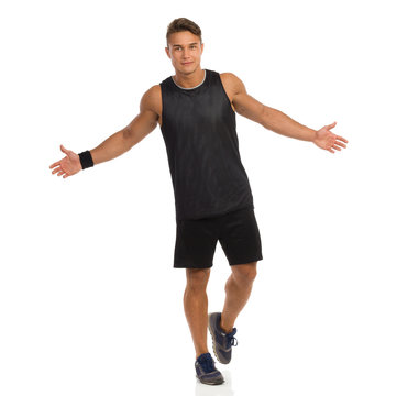 No Problem. Young Man In Sport Black Shirt And Shorts Walking With Arms Outstretched. Front View. Full Length Studio Shot Isolated On White.