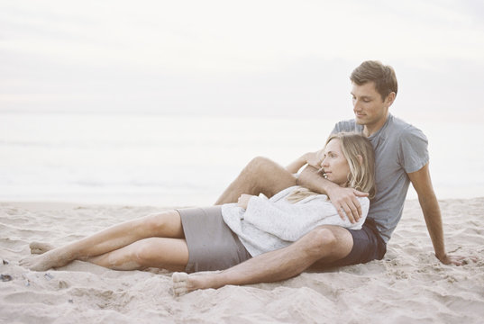 A couple sitting close on a beach, a man and woman with their arms around each other and heads together.