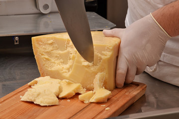 Cocinero cortando trozos de queso parmesano. 
