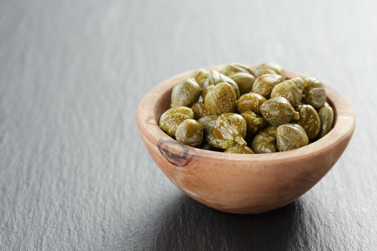 marinated capers in olive bowl on slate board with copy space