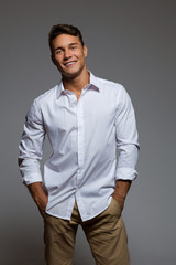 Relaxed Male Model. Smiling handsome man in white shirt posing with hands in pockets. Three quarter...