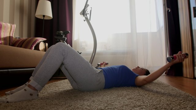 Woman exercising with dumbbells in home, dolly shot