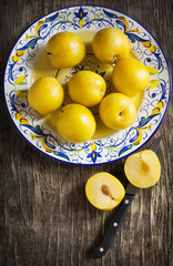Fresh yellow plums in a plate on wooden background