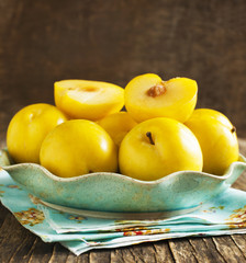 Fresh yellow plums in a plate on wooden background