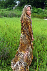 Attractive blond fashion model posing at grass field wearing animal print resort dress.