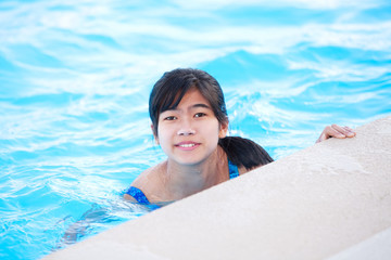 Young teen girl relaxing in pool, smiling at camera