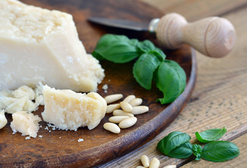 Parmesan auf Holzbrett - Holztisch mit Parmesanmesser, Basilikum und Pinienkernen