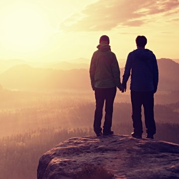 Couple in love enjoying tender moments during sunset . Young pair of hikers hand in hand on the peak of rock empires park and watch over the misty and foggy morning valley to Sun.
