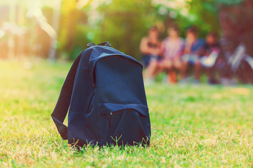 Blue school backpack standing on green grass with students in ba