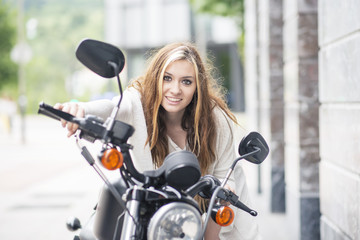 Fototapeta na wymiar Cheerful young woman on the classic motorcycle in the street.