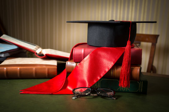 Graduation Cap And Red Ribbon Lying On Books At Library