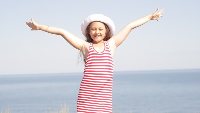 girl in white hat stands on the sea beach arms outstretched