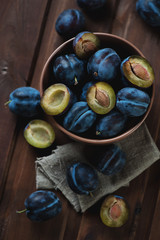 Above view of a glass bowl with plums, dark brown wooden surface
