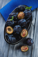 Enameled bowl with ripe plums over grey wooden surface, close-up