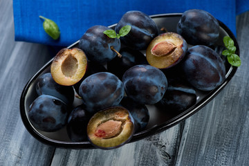 Bowl with plums over grey wooden background, above view