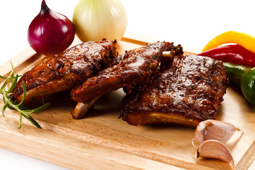 Barbecued ribs with vegetables on cutting board 
