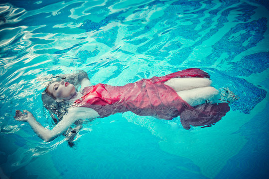 Young sexy woman floating on swimming pool in red dress. beauty shot