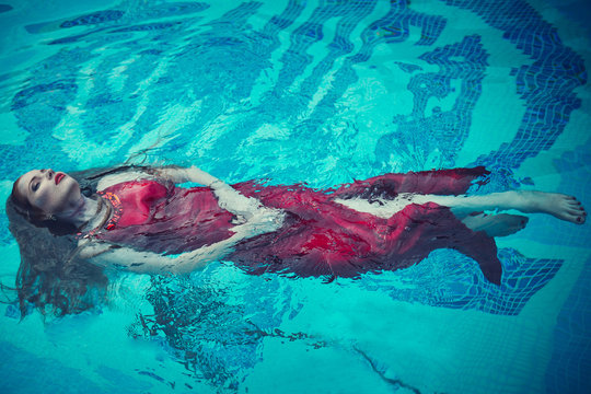 Young sexy woman floating on swimming pool in red dress. beauty shot