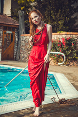 Young sexy woman floating on swimming pool in red dress.