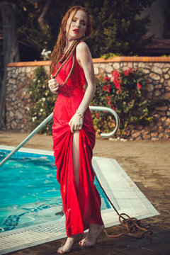 Young sexy woman floating on swimming pool in red dress.
