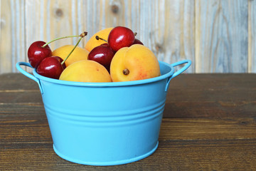 Fruit bowl. Sweet cherries and apricots in a blue metal bowl on wooden table                           