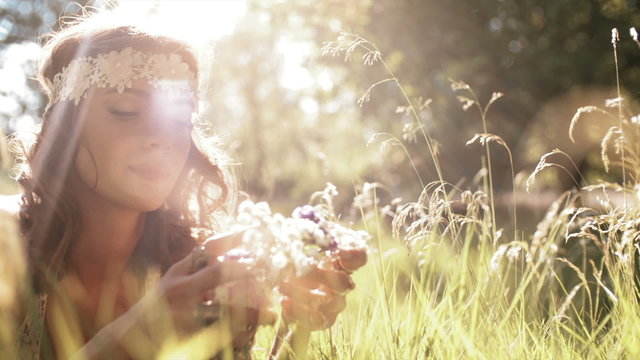 Smiling hippie girl lying in grass holding wild flowers 