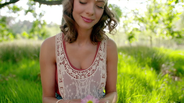 Boho girl smiling and holding a flower in a park