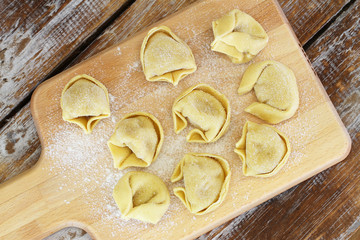 Uncooked tortellini laid out on wooden board
