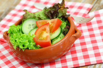 Green salad in clay bowl on checkered napkin
