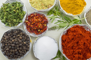 Various spices in shiny bowls on a white wooden table close up