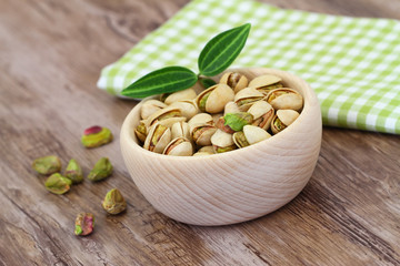 Pistachio nuts in wooden bowl on checkered cloth
