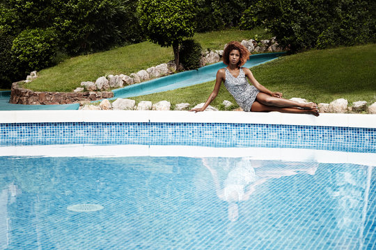 woman in coctail dress sitting on a board of pool