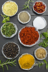 Various spices in shiny bowls on a dark wooden table