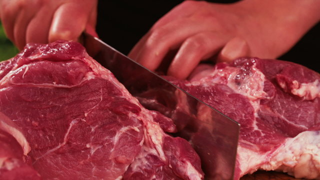 Large piece of raw pork being cut with a cleaver