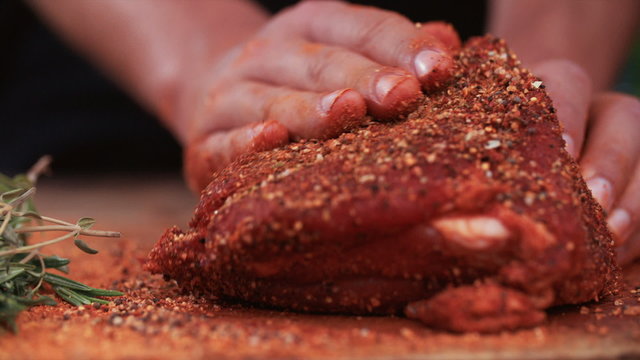 Seasoning of herbs and spices being rubbed into pork
