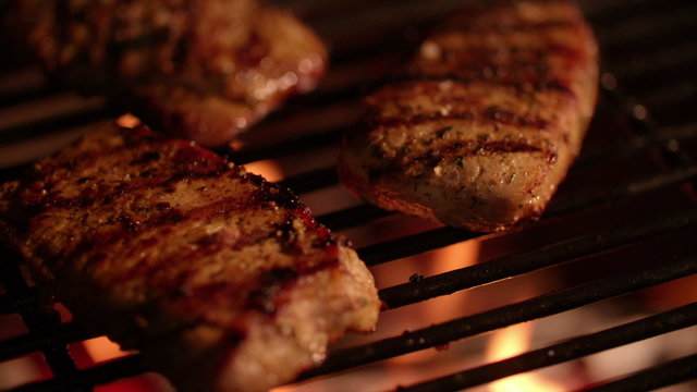Chicken fillets being flame grilled on a barbecue at night