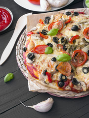 pizza with tomatoes, mushrooms, olives and peppers served on a wooden table