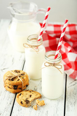 Two bottles of milk with striped straws and cookies on white wooden background