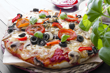 pizza with tomatoes, mushrooms, olives and peppers served on a wooden table