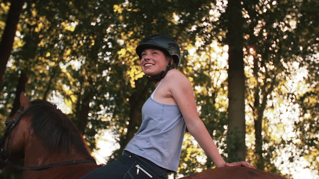 Girl riding her horse down a sunlit park lane
