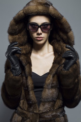 Sexy Beauty Girl with natural  Make up.  Fashion Brunette  Portrait of a girl dressed in fur coat,  black dress and sunglasses posing on a grey background. Retro style