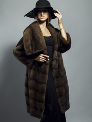 Sexy Beauty Girl with natural  Make up.  Fashion Blonde Portrait of a girl dressed in fur coat and black hat posing on a grey background. Retro style. 