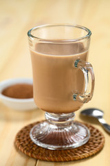 Hot chocolate with cocoa powder and spoon in the back  (Selective Focus, Focus on the front rim of the glass)