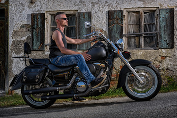 Fototapeta na wymiar Tough guy with his bike in front of an old house