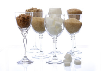 Different types of sugar in glasses on white.