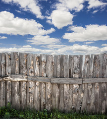 Old wooden fence against blue sky with clouds