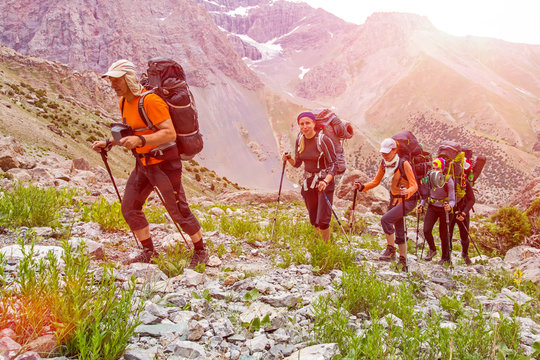Extreme climbers scrambling up.
Group people approach high altitude mountain climbing camp with heavy backpacks tons alpine gear walking on rocky path trail at peaks glaciers snow sun sky background