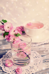 Beautiful fruit blossom in glass and tea cup on table on light background