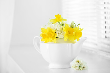 Beautiful bouquet of yellow daffodils and roses in teapot on windowsill