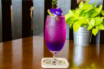 Juice of Butterfly pea with lemon and ice in glass on wooden table. Herb drink for refreshment.